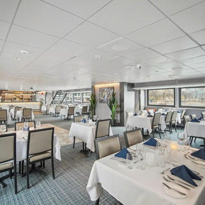 A modern dining room with neatly set tables, white tablecloths, and blue napkins, located in a bright and spacious area.