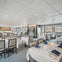 A spacious, modern restaurant with neatly set tables, white tablecloths, blue napkins, and large windows overlooking a scenic view.