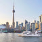 A city skyline featuring a tall tower and modern buildings, with a white boat on a body of water in the foreground.