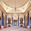 Opulent hall with chandeliers, large mirrors, blue columns, red chairs, and ornate gold detailing on the domed ceiling and walls.