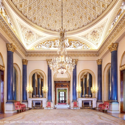 Opulent hall with chandeliers, large mirrors, blue columns, red chairs, and ornate gold detailing on the domed ceiling and walls.