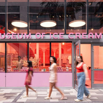 Three people walk past the entrance of the Museum of Ice Cream, which has pink signage and large glass windows.