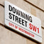 A street sign reading 'Downing Street SW1, City of Westminster' mounted on a beige wall.