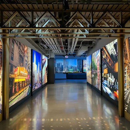 A corridor with illuminated cityscape photos on both walls, leading to a room with a city skyline visible through the window.
