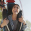 A woman smiling while riding an amusement park ride with another person visible in the background.