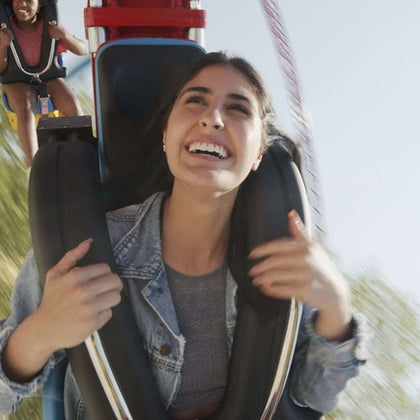 A woman smiling while riding an amusement park ride with another person visible in the background.