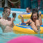 People enjoying themselves in a water park. A young woman is in a yellow inflatable tube, splashing water and smiling.