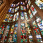 Ornate stained glass windows with various colorful designs in a cathedral, featuring a detailed cross in the foreground.