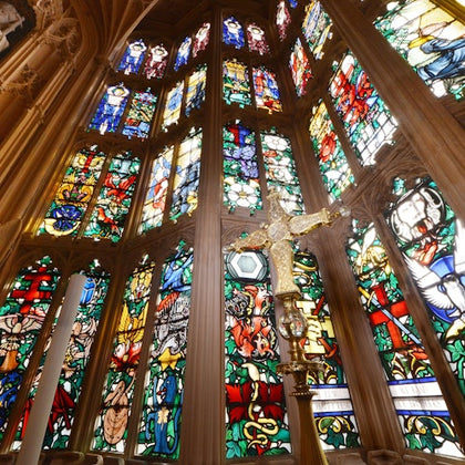 Ornate stained glass windows with various colorful designs in a cathedral, featuring a detailed cross in the foreground.