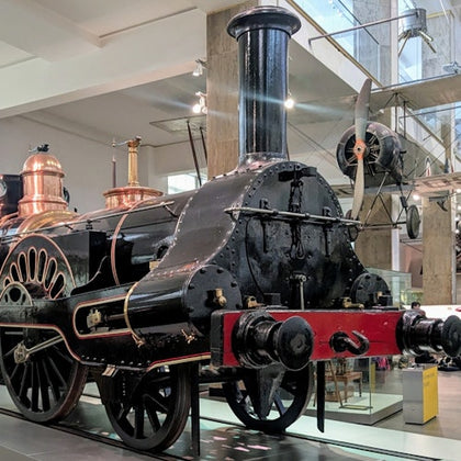 A historic steam locomotive displayed indoors, featuring black and red colors with copper details, in a museum setting.