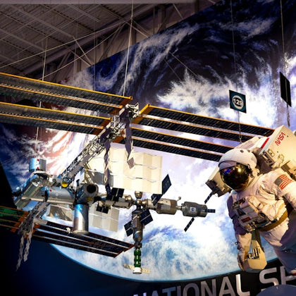 A model of the International Space Station and an astronaut suit on display in a museum, with Earth depicted in the background.