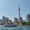 A ferry on water with a city skyline in the background, featuring the CN Tower and various buildings under a clear sky.