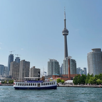 A ferry on water with a city skyline in the background, featuring the CN Tower and various buildings under a clear sky.