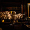 A grand wooden owl statue with outstretched wings is displayed in a dimly lit library, surrounded by bookshelves and candles.