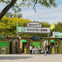 Entrance to the Toronto Zoo with signs, ticket booths, and visitors under a clear sky surrounded by greenery.