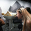 A woman looks through a mounted telescope in a museum with a black-and-white cityscape background.
