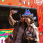 Two people smiling while taking a selfie in front of a colorful tour bus on a sunny day.