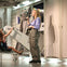 A woman speaks into a microphone in a futuristic room with equipment, while a child interacts with a seated device to her left.