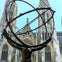 A sculpture of Atlas holding an armillary sphere in front of a gothic-style cathedral under a clear blue sky.