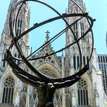A sculpture of Atlas holding an armillary sphere in front of a gothic-style cathedral under a clear blue sky.