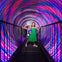 Two girls stand on a bridge inside a tunnel with swirling, colorful lights.