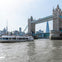 A boat passes under Tower Bridge in London on a sunny day, with the Shard visible in the background.