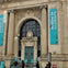 Facade of the Museum of Illusions with a grand arched entrance and banners advertising the museum.