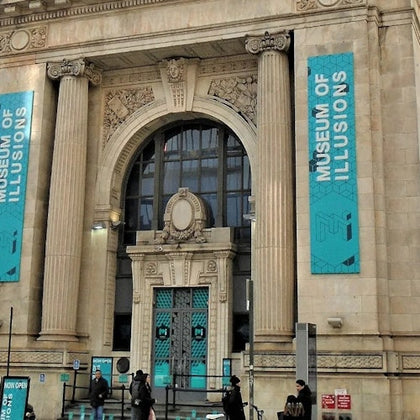 Facade of the Museum of Illusions with a grand arched entrance and banners advertising the museum.