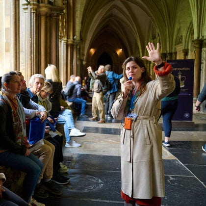 A tour guide speaking to a seated group in a historic building with vaulted ceilings and Gothic architecture.