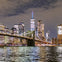 A nighttime cityscape featuring a lit bridge and skyscrapers reflecting on the water.