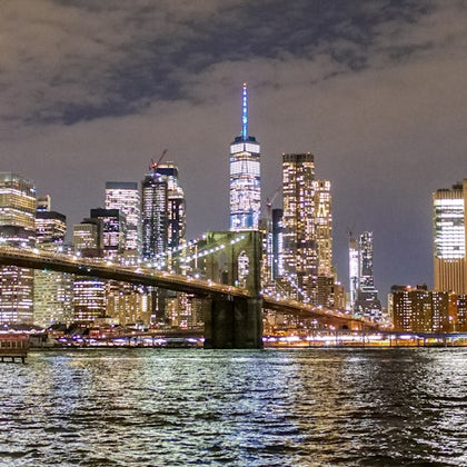 A nighttime cityscape featuring a lit bridge and skyscrapers reflecting on the water.