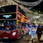A red double-decker bus with "City Sightseeing London" displayed, decorated streets with lights, and pedestrians at night.