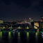 A cityscape at night showing a river, illuminated bridges, and buildings with lit windows and lights in the distance.