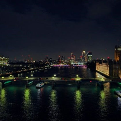 A cityscape at night showing a river, illuminated bridges, and buildings with lit windows and lights in the distance.