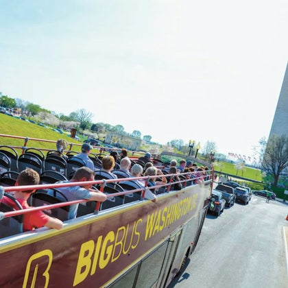 A double-decker sightseeing bus labeled "BIG BUS WASHINGTON" with passengers, near the Washington Monument and flags.