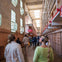 Visitors wearing headphones explore a prison interior with barred cells and tall windows, guided by an audio tour.