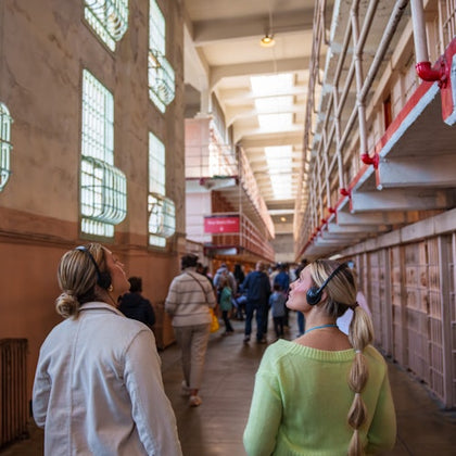 Visitors wearing headphones explore a prison interior with barred cells and tall windows, guided by an audio tour.
