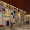 A large abstract mural with geometric shapes in red, blue, yellow, and white in a modern indoor setting with a person nearby.