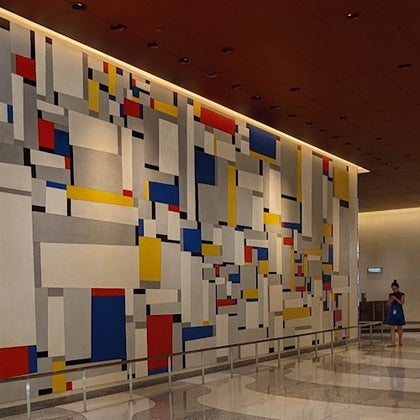 A large abstract mural with geometric shapes in red, blue, yellow, and white in a modern indoor setting with a person nearby.