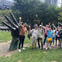 A group of people posing with a large hand sculpture in a park, with trees and buildings in the background.