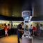 People in a museum exhibit interacting with a display labeled 'Touch the Moon,' with other exhibits visible in the background.