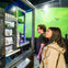 Two individuals observe a detailed miniature model of a building in a display case, with a green-lit backdrop showing flying creatures.