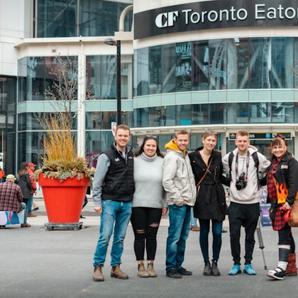 Six people stand together outside the Toronto Eaton Centre. Large planter with tall grass is visible.