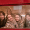 A group of five smiling people seen through the window of a red vehicle, holding drinks and appearing cheerful.