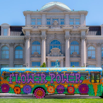 A vibrantly painted bus with the words "Flower Power" parked in front of a classical-style building with columns.