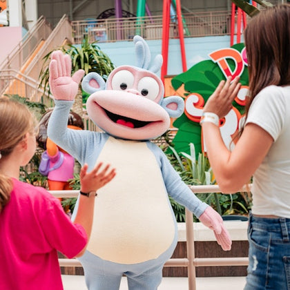 A person in a cartoon monkey costume high-fiving two children in a colorful indoor play area.