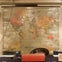 A vintage world map is mounted on a wall above a table with an old red toolbox, chairs, and a sign.