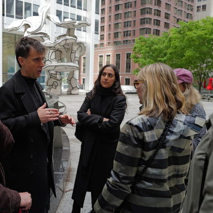 A group of people having a discussion in an outdoor urban setting with modern art sculptures and trees in the background.