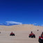 People riding red ATVs across a vast, sandy desert under a bright blue sky.