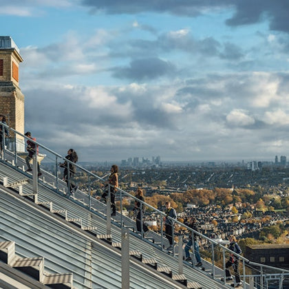People walking on an outdoor staircase with a cityscape and cloudy sky in the background.
